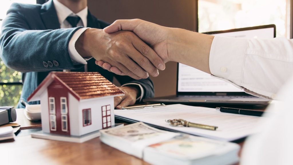 two people shaking hands over a house model-Real Estate Sales LLC