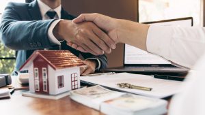 two people shaking hands over a house model-Real Estate Sales LLC